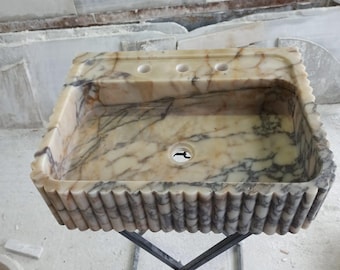 May include: A white marble sink with a fluted edge and three holes on the top. The sink is on a black metal stand.
