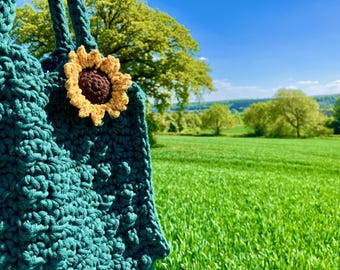 Niepowtarzalna torba na jednodniową wycieczkę z brelokiem w kształcie słonecznika, wykonana z włóczki pochodzącej z recyklingu przez firmę Campfire Crochet.