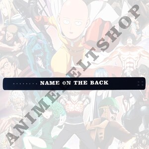 Pode incluir: Cinto preto com texto branco que diz "NAME ON THE BACK". O cinto &eacute; mostrado contra um fundo de personagens de anime.