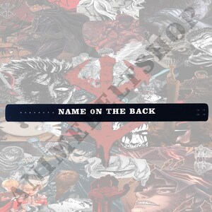 May include: A black leather wristband with white stitching and the text "NAME ON THE BACK" printed in white.