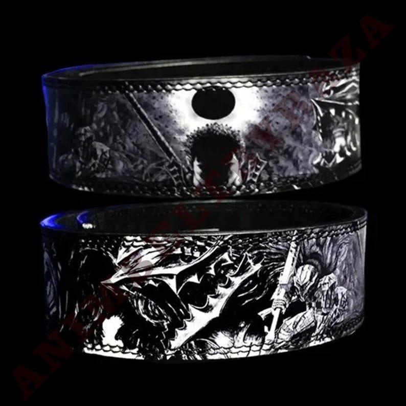 May include: Two black leather belts with a white and black graphic print of a character from the anime series Berserk. The top belt features a character with a sword and a full moon in the background. The bottom belt features a character with a sword and a dragon in the background.