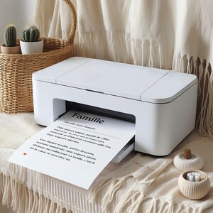 May include: A white printer with a sheet of paper feeding through it. The paper has a black and white text print that reads "Famille" with a French definition of the word. The printer is sitting on a white surface with a wicker basket and two small white ceramic containers.