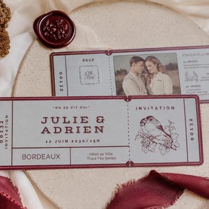 Peut inclure: Cartes d'invitation de mariage avec un design de billet vintage. Les cartes présentent les noms "Julie & Adrien", la date et le lieu. Une carte comporte une photo d'un couple, et l'autre une illustration d'oiseau. Un sceau de cire bordeaux et un ruban sont également présents.