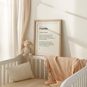 May include: A framed print with the word "Famille" in a simple black font. The print is in a light wood frame and is hanging on a white wall. The text below the word "Famille" is in French and defines the word as a family.