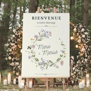 Peut inclure: Une pancarte de bienvenue de mariage blanche avec une couronne de fleurs et le texte "BIENVENUE à notre Mariage Marie & Marius".