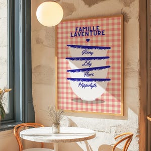 Peut inclure: Une affiche à carreaux rose et blanc avec le texte "Famille Laventure" et un symbole de cœur. Quatre bols blancs sont empilés les uns sur les autres avec une bordure bleue et les noms "Ginny", "Lily", "Flore" et "Hippolyte" écrits en bleu sur chaque bol.