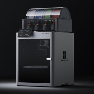 May include: A silver and black 3D printer with a clear top section containing coloured filament spools. The printer has a small screen and the text "Bambu Lab" is visible on the side. The model name is P1S.