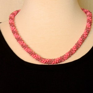 May include: A pink and mauve beaded necklace with a twisted design.