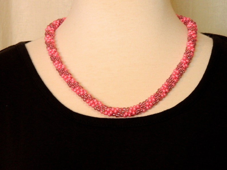 May include: A pink and mauve beaded necklace with a twisted design.