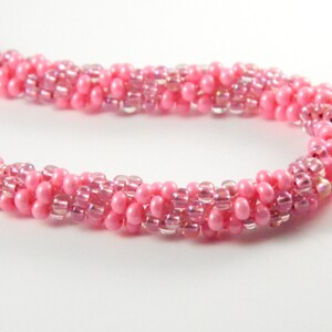 May include: A pink beaded necklace with a twisted design. The beads are a mix of iridescent and solid pink.