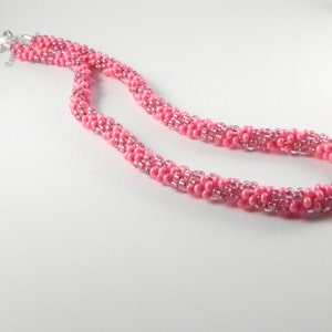 May include: A pink beaded necklace with a silver clasp. The necklace is made of small, round beads that are arranged in a spiral pattern.