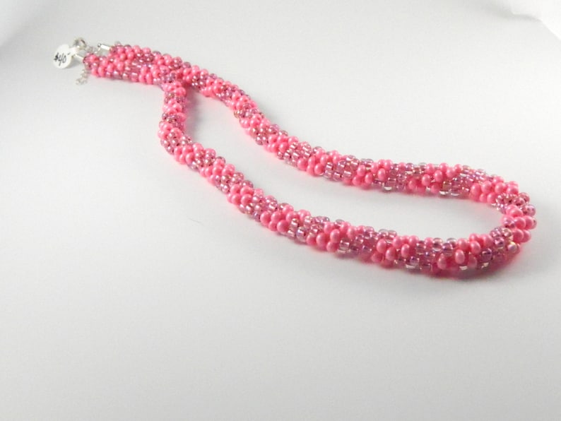 May include: A pink beaded necklace with a silver clasp. The necklace is made of small, round beads that are arranged in a spiral pattern.