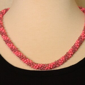 May include: A pink and mauve beaded necklace with a twisted design.