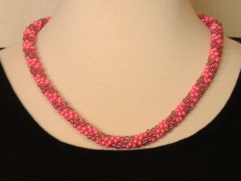 May include: A pink and mauve beaded necklace with a twisted design.
