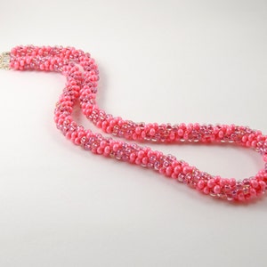 May include: A pink beaded necklace with a silver clasp. The necklace is made of small, round beads that are strung together in a spiral pattern.