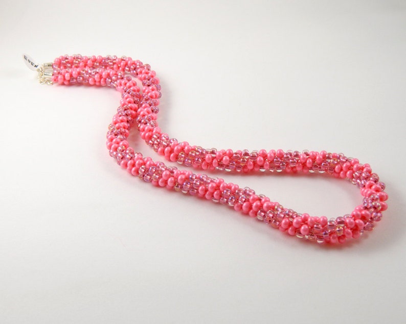 May include: A pink beaded necklace with a silver clasp. The necklace is made of small, round beads that are strung together in a spiral pattern.