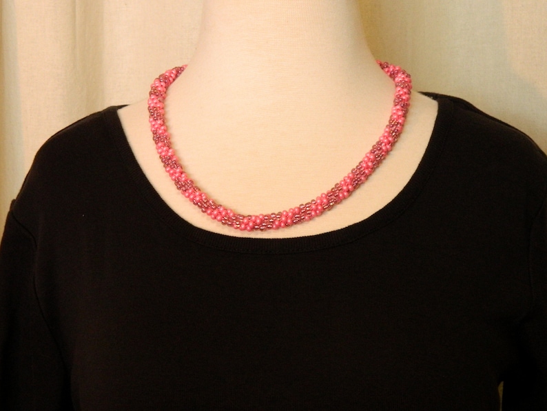 May include: A pink beaded necklace with a twisted design. The necklace is worn on a black shirt.
