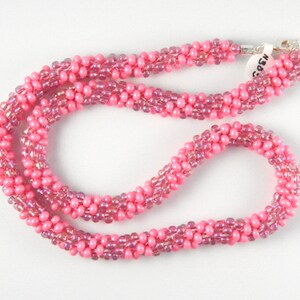May include: A pink beaded necklace with a silver clasp. The beads are iridescent and have a subtle shimmer.