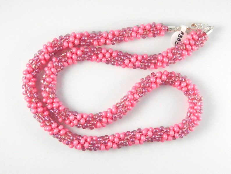 May include: A pink beaded necklace with a silver clasp. The beads are iridescent and have a subtle shimmer.