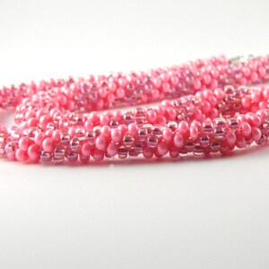 May include: A pink beaded necklace with a spiral design. The beads are iridescent and have a subtle shimmer.
