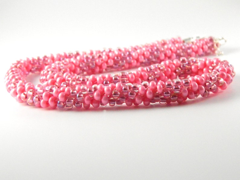 May include: A pink beaded necklace with a spiral design. The beads are iridescent and have a subtle shimmer.