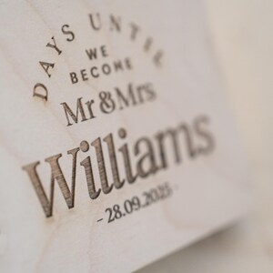 May include: Close-up of a wooden sign with the text "Days Until We Become Mr & Mrs Williams - 28.09.2023".