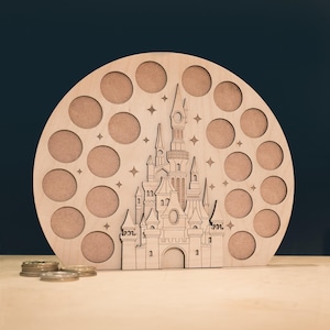 May include: A wooden, circular display with 17 circular openings and a castle silhouette. The castle is intricately cut out of the wood, with stars etched around it. A few coins are visible in the foreground. The display is made of light-colored wood.
