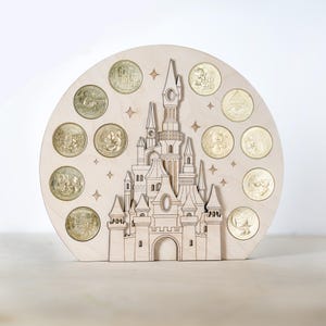 May include: A wooden cutout of a castle with a circular base. The castle is surrounded by 12 gold coins with various Disney characters on them. The background is a light wood colour.