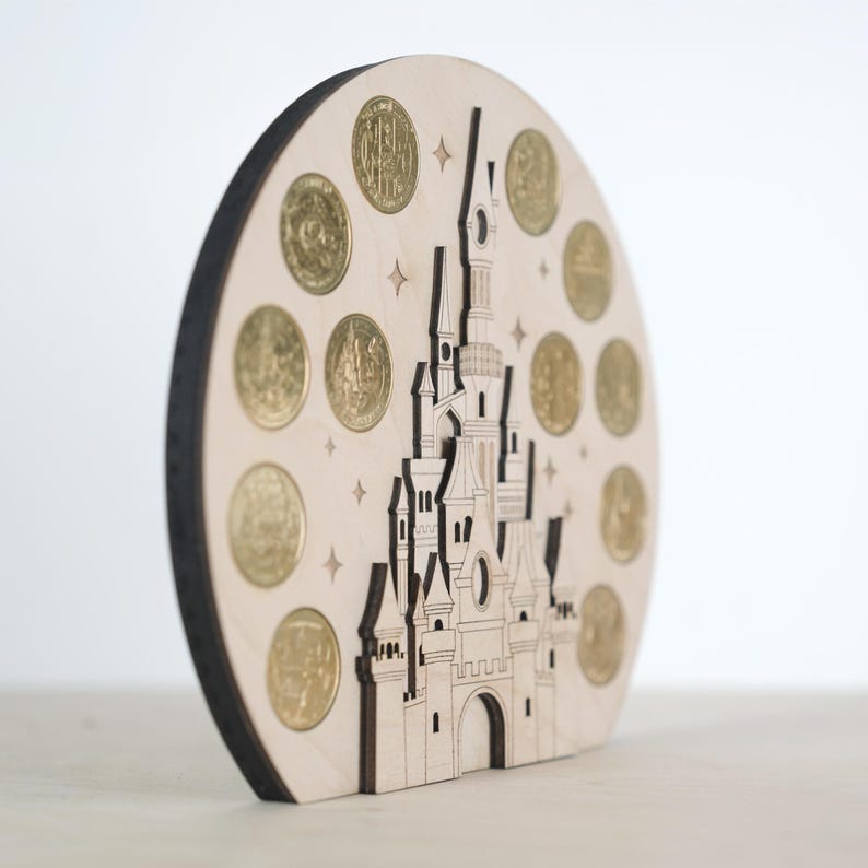 May include: A wooden cutout of a castle with a circular base. The castle is decorated with gold coins and stars. The castle is a light brown colour and the coins are a shiny gold colour.