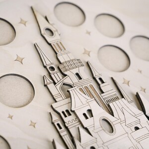 May include: A wooden cutout of a castle with intricate details, set against a background of stars. The castle has multiple towers and windows, and the design is reminiscent of a fairytale.