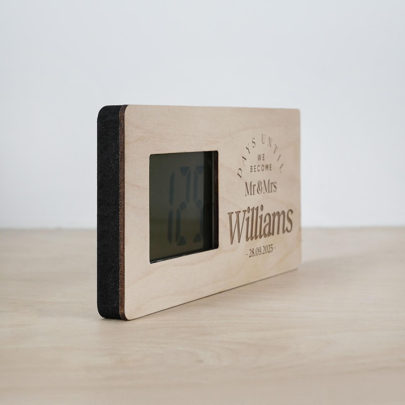 May include: A wooden countdown clock with a digital display showing the number of days until a wedding. The clock is engraved with the text "Days Until We Become Mr & Mrs Williams - 28.09.2025".