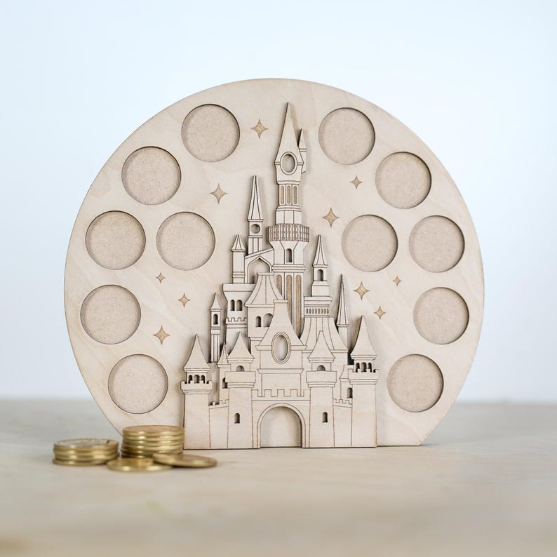 May include: A wooden coin bank shaped like a castle with a circular base and 12 coin slots. The castle is detailed with towers, windows, and a pointed roof. The bank is painted in a light wood colour.