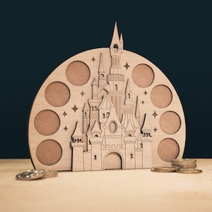 May include: A wooden castle-shaped coin holder with a semi-circular design. The castle has intricate details, including towers, windows, and a central arched entrance. Eight circular openings are arranged around the castle. Several coins are visible in front of the holder.