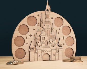 May include: A wooden castle-shaped coin holder with a semi-circular design. The castle has intricate details, including towers, windows, and a central arched entrance. Eight circular openings are arranged around the castle. Several coins are visible in front of the holder.