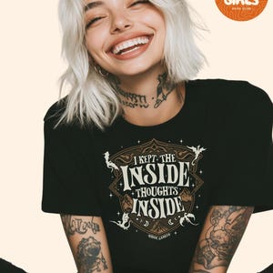 May include: Black t-shirt with the text "I KEPT THE INSIDE THOUGHTS INSIDE" in a decorative design. The shirt also features the text "RIDOC GAMLYN". A round orange logo in the upper right corner reads "SAD GIRLS BOOK CLUB".