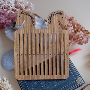 May include: Wooden loom with two horse head designs at the top. The loom has 10 slots for weaving.