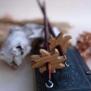 Könnte beinhalten: Holzspindeln mit Sternmuster. Die Spindeln haben einen dunkelbraunen Schaft und einen hellbraunen, sternförmigen Wirtel. Die Spindeln liegen auf einem dunkelblauen Buch mit goldfarbenen Prägungen.