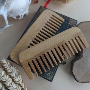 May include: Two wooden combs made of bamboo, stacked on top of each other. The combs are on a book with a dark blue cover and gold accents.