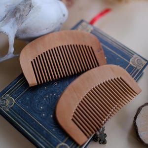May include: Two wooden combs with a curved shape and fine teeth. The combs are on top of a blue book with a gold design.