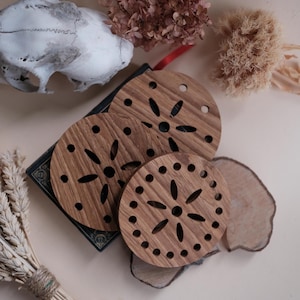 May include: Three round wooden coasters with a carved floral design. The coasters are stacked on top of each other and are made of light brown wood.