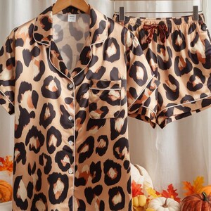 May include: A leopard print pajama set. The set includes a short-sleeved shirt with a chest pocket and matching shorts. The shirt has buttons and white trim. The pajamas are in shades of tan, brown, and black. The shorts have a drawstring.