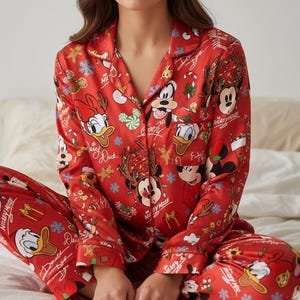 May include: Red pajama set featuring a print of Mickey Mouse, Donald Duck, and other Disney characters in a Christmas theme. The long-sleeved top and pants are made of a silky material. The pajama set has a button-down top and a relaxed fit.