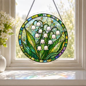 Pu&ograve; includere: Un acchiappasole circolare in vetro colorato raffigurante fiori bianchi di mughetto con foglie verdi su uno sfondo strutturato. Il pezzo &egrave; incorniciato da un bordo decorativo di piccoli segmenti di vetro verde, blu e giallo e pende da una catena.