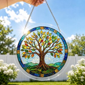 Pu&ograve; includere: Un acchiappasole circolare con un design dell'albero della vita in stile mosaico, con un tronco marrone e foglie multicolori nelle tonalit&agrave; del giallo, arancione e verde. Il bordo &egrave; blu con accenti dorati ed &egrave; appeso a una catena di metallo argentato.