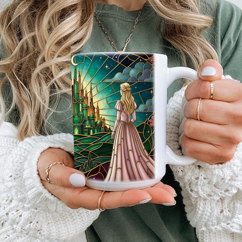 Puede incluir: Taza de cer&aacute;mica blanca con una ilustraci&oacute;n estilo vidriera. El dise&ntilde;o representa a una mujer con un vestido rosa mirando un castillo verde bajo un cielo estrellado. Los detalles dorados enmarcan la obra de arte, creando un tema caprichoso y de cuento de hadas.