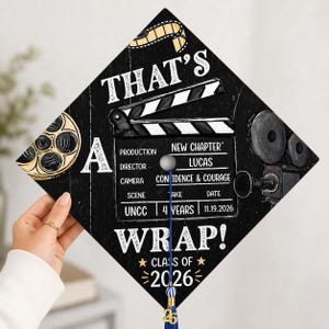Könnte beinhalten: Ein schwarzer Abschlusskappen-Topper mit Filmmotiv, bestehend aus Filmklappe, Filmrolle und Vintage-Kamera. Der Text lautet: THAT'S A WRAP! NEW CHAPTER, LUCAS, CONFIDENCE & COURAGE, UNCC, 4 YEARS, 11.19.2026, CLASS OF 2026. Inklusive einer blauen Quaste.