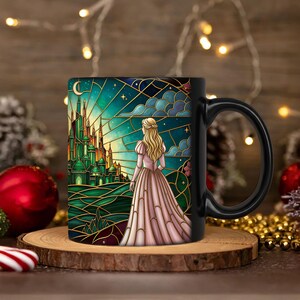 Puede incluir: Taza de cer&aacute;mica negra con una ilustraci&oacute;n de estilo vidriera de una mujer con un vestido rosa mirando un castillo verde bajo un cielo estrellado. La taza tiene un asa negra y est&aacute; sobre una superficie de madera.