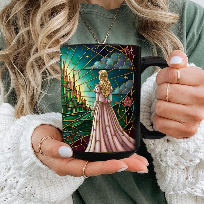 Puede incluir: Taza de cer&aacute;mica negra con un dise&ntilde;o de vidriera que representa a una mujer con un vestido rosa contemplando un castillo verde. La obra de arte incluye un cielo estrellado y detalles dorados. La taza tiene un asa negra.