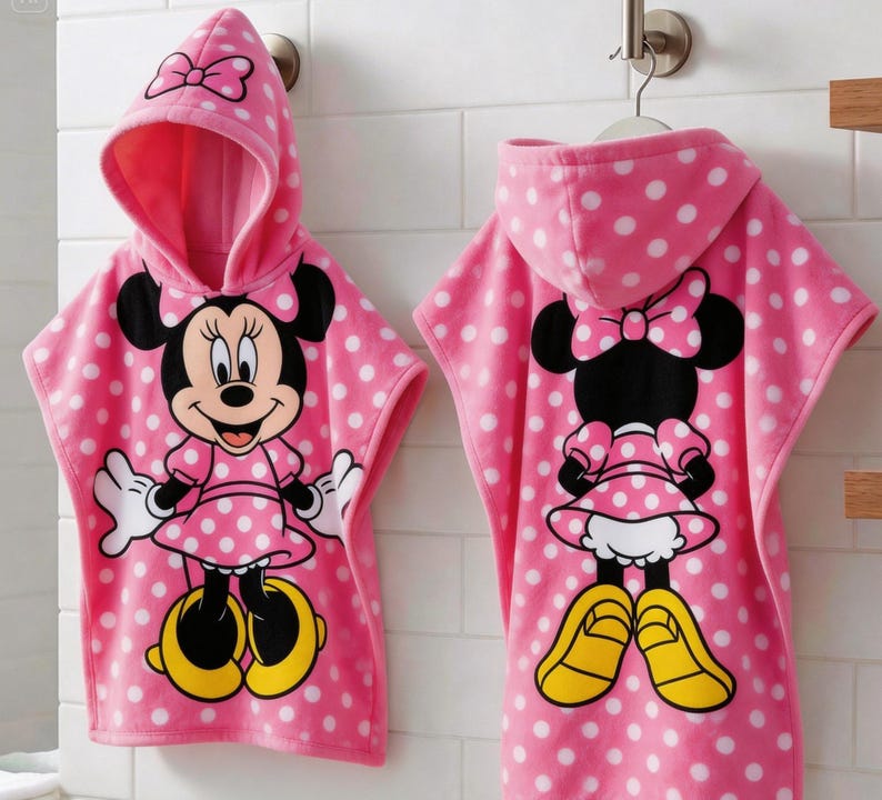 May include: Pink hooded towel with white polka dots and a Minnie Mouse graphic. The towel features a hood with a bow and a large Minnie Mouse character on the front. The back of the towel also features a Minnie Mouse graphic.