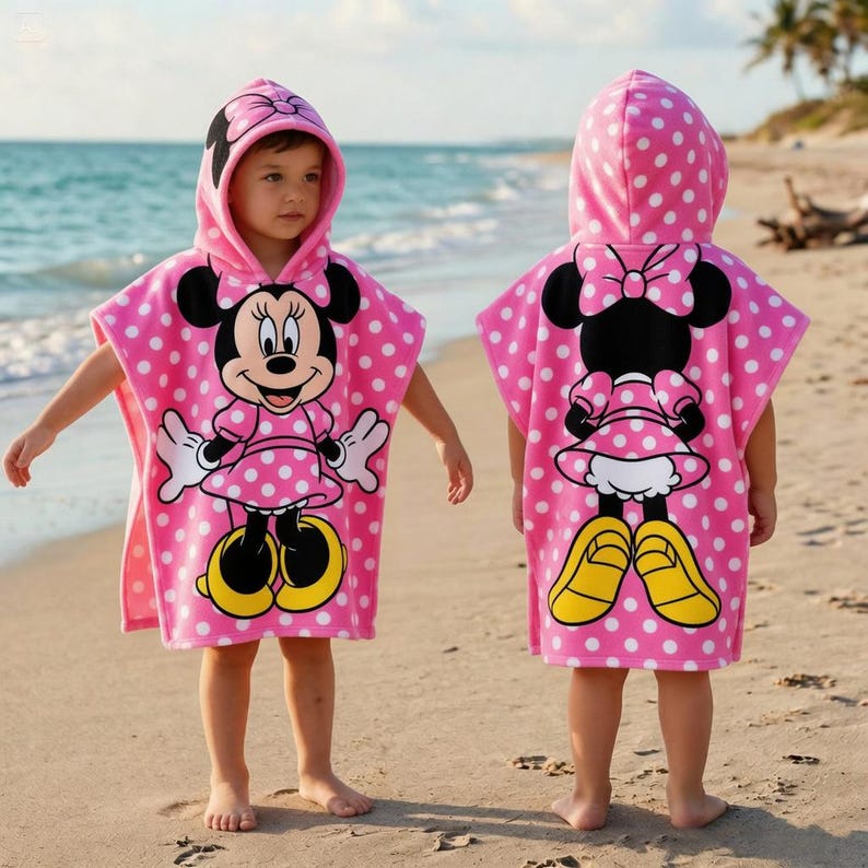 May include: Pink hooded beach towel with white polka dots and a Minnie Mouse graphic. The towel features a large Minnie Mouse character on the front and back, with yellow shoes and a bow. The towel is designed for children.